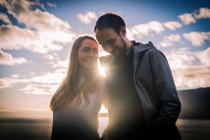 A couple shares an intimate moment against a dramatic sunset sky with clouds.
