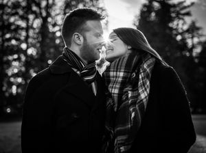 A couple in winter coats shares a tender black and white moment outdoors.