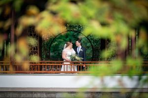 A couple seen through foliage on a garden bridge during their wedding day.
