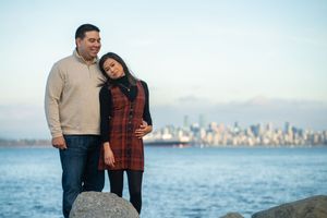 A couple poses for engagement photos with the Vancouver skyline and waterfront in the background.