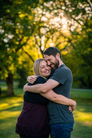 A couple shares a warm embrace in a park during golden hour.