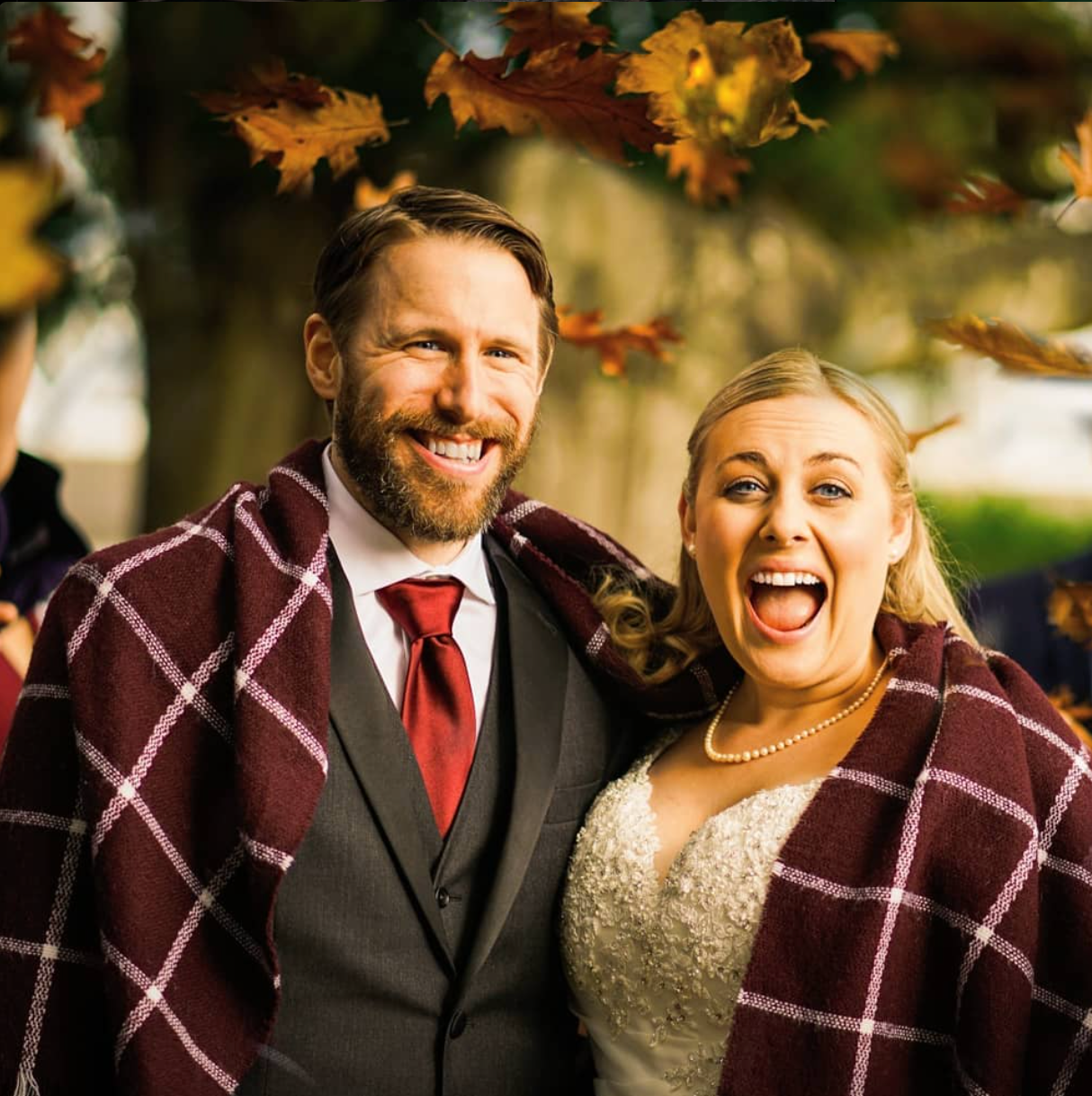 A happy couple sharing a romantic autumn moment outdoors with a plaid blanket and formal attire.