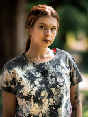 Young person wearing a tie-dye patterned t-shirt with black and beige colors poses outdoors in natural lighting.