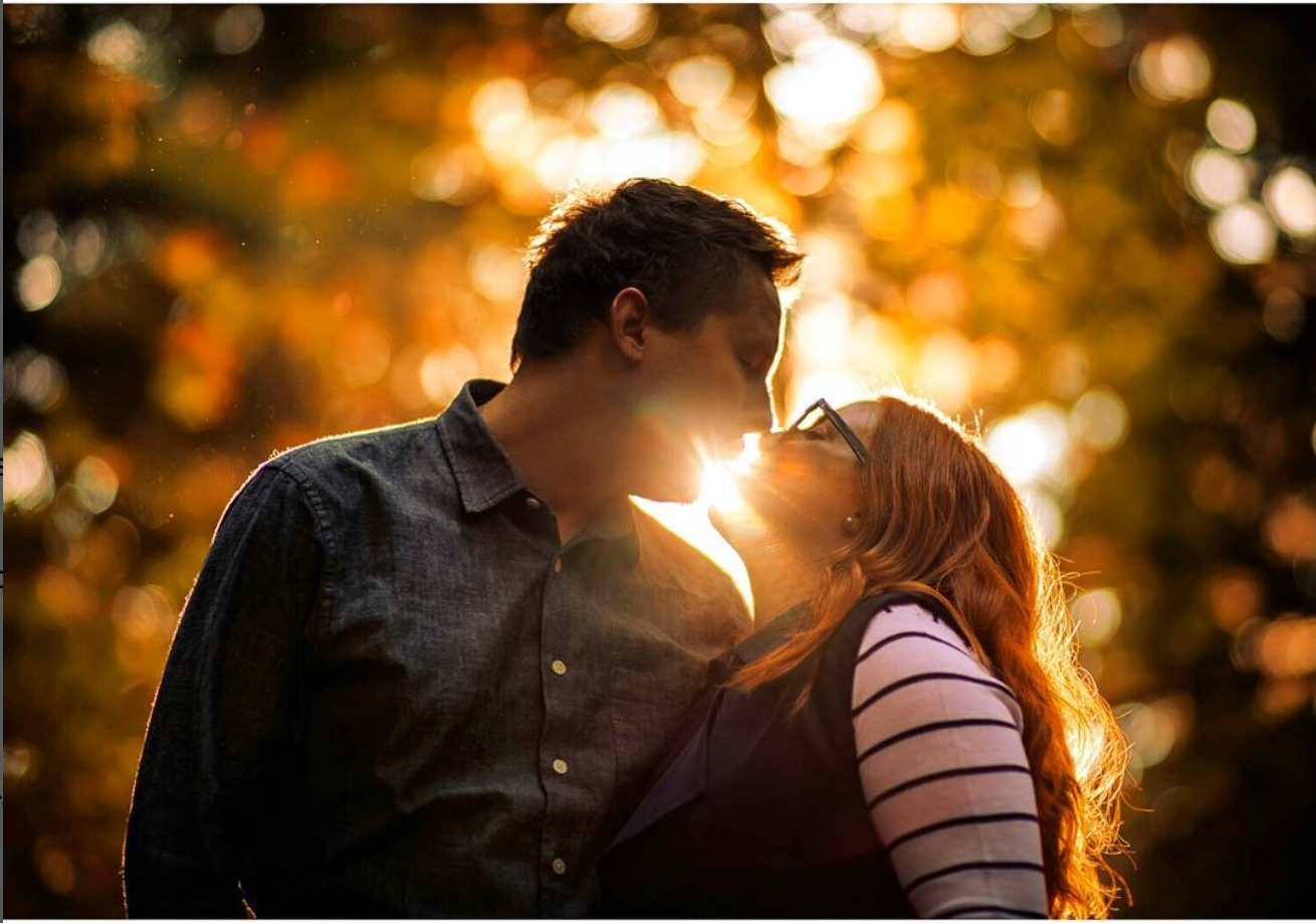 A couple embraces in golden sunset light with bokeh and lens flare creating a dreamy romantic atmosphere.