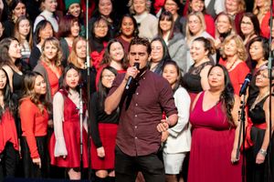 A large choir group performs in red attire on stage during a concert performance.