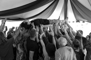 Crowd lifts and supports someone crowd surfing under a draped tent ceiling.