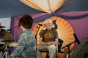 Performers on stage under a colorful tent canopy at an outdoor festival.