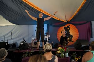 Performers on stage lead an audience under a decorated tent with dramatic orange lighting.