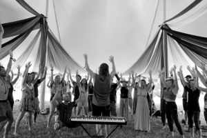 Black and white photo of people with raised arms during a musical performance under a tent.