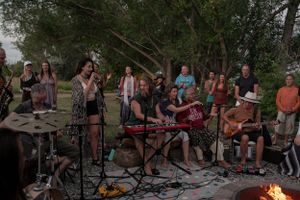 Musicians perform outdoors with instruments and equipment setup around a campfire.