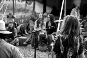 Musicians perform at outdoor concert with audience seated on ground in black and white.