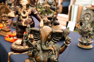 Ornate metal Ganesh statues and decorative figures displayed on dark table at market.