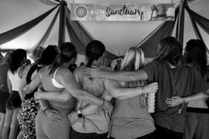 Black and white image of festival attendees embracing in a circle under the Sun Sanctuary banner.