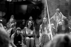 An engaged audience watches an outdoor performance seated on blankets in black and white.