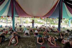 Large group doing yoga poses under a multicolored canopy tent outdoors.