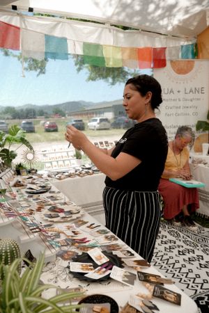 Vendor arranging merchandise at a craft fair booth decorated with colorful bunting.