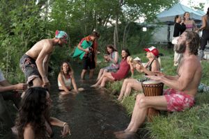 A group relaxes by a river bank during an outdoor summer gathering with musical instruments.