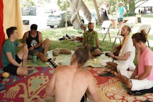 A group of people sitting in a circle on blankets with musical instruments under trees.