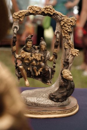 Decorative bronze sculpture showing figures on an ornate swing with floral designs.