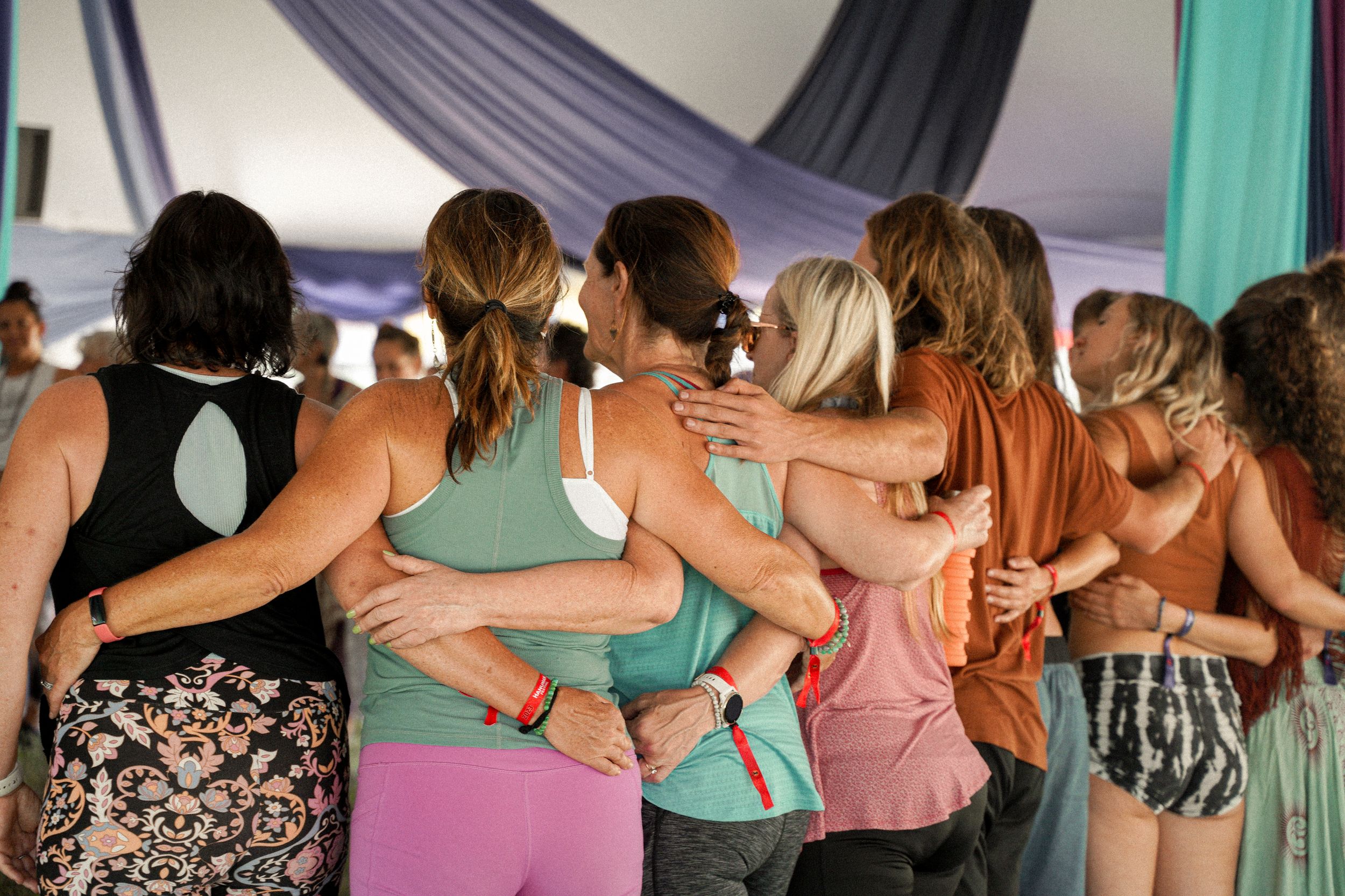 Festival participants stand in a close line with arms around each other under a decorated tent.