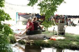 People relax in hammocks by a stream during a sunny summer day outdoors.