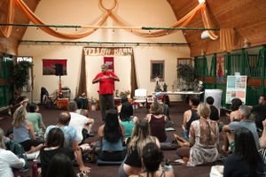 A group meditation or workshop session with participants seated on the floor in an indoor space.