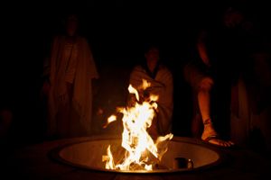 People gather around a bright fire pit in the darkness.