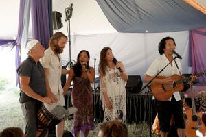Band members perform together on stage under a tent with draped fabric decorations.