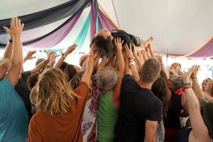 Participants raise their hands in unison during an energetic group activity under a decorated tent.