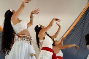 Dance performers in flowing white costumes with red sashes moving gracefully with raised arms.