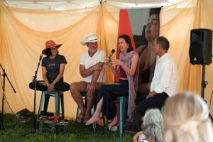 Musicians performing on stools under a tent canopy at an outdoor festival.