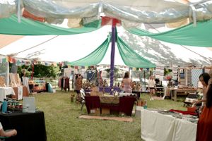 View of a large tented marketplace with vendor tables and green and white draped ceiling.