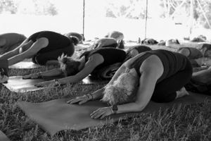 People in child's pose on yoga mats during an outdoor class.