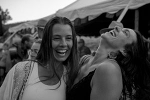 Two friends share a joyful moment of laughter together at an outdoor event under a tent.