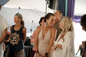 People gather in casual white clothing at an indoor event with draped fabric decor.