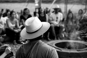 Person in hat watches performance near fire pit with audience in background.