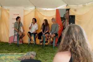 People engage in conversation while seated on stools at an outdoor gathering with draped fabric backdrops.