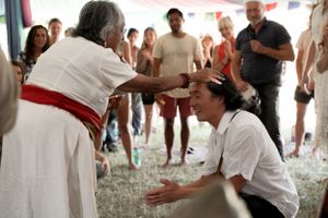 Two people interact during a ceremonial moment at an indoor festival event.