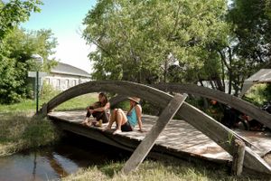 People lounging on an arched wooden bridge over a small stream.