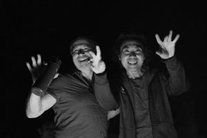 Two figures making playful expressions and waving hands at the camera in a black and white photo.