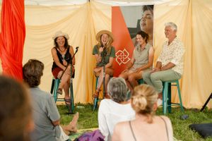 Speakers engage in discussion on stage at an outdoor festival event under a draped tent.