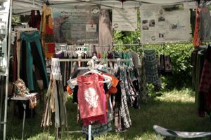 A vendor booth at an outdoor market displays clothing and merchandise hanging under a canopy tent.