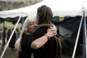 Two people share an emotional embrace under a white tent.
