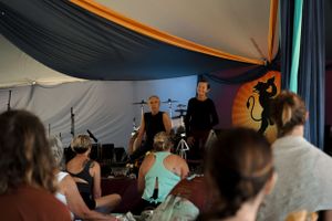 A performance takes place in a tent with colorful fabric draping and stage lighting.