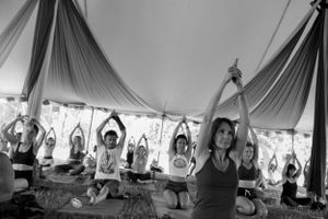 People practicing yoga with raised arms in a draped festival tent.