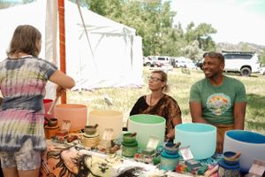 Vendors display colorful ceramic bowls and handmade items at an outdoor craft market.