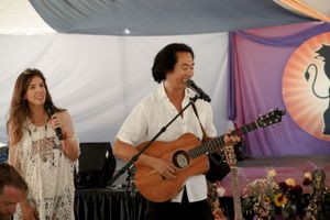 Musicians perform with acoustic guitar under a decorated festival tent with fabric draping.