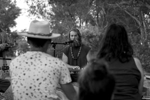 Musicians perform for a small gathering under trees at an outdoor event.