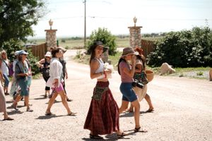 A crowd walks along a dusty path near stone pillars during an outdoor event.