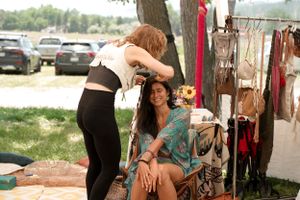 Two vendors interact at a market stall with clothing and accessories displayed in background.